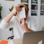 Empresária mostra um recibo enquanto trabalha em um computador no home office.