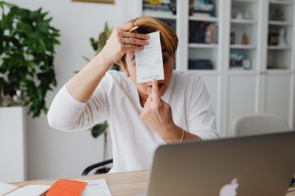 Empresária mostra um recibo enquanto trabalha em um computador no home office.