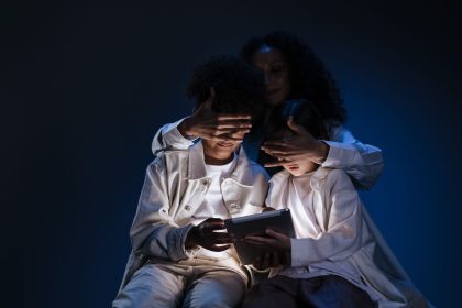 Mãe acompanha duas crianças enquanto elas usam um tablet em casa.