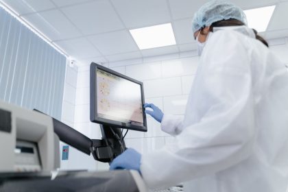 Pesquisadora de jaleco utiliza um monitor touchscreen em um laboratório moderno.