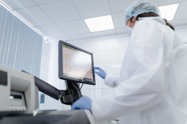Pesquisadora de jaleco utiliza um monitor touchscreen em um laboratório moderno.