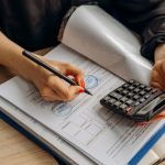 Contador usa uma calculadora e assina documentos financeiros sobre uma mesa de trabalho.