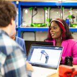 Equipe diversificada de profissionais colaborando em um projeto de inovação em um escritório moderno, com laptops e modelos tridimensionais.