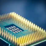 Close de um chip de processador com pinos dourados sobre fundo azul.