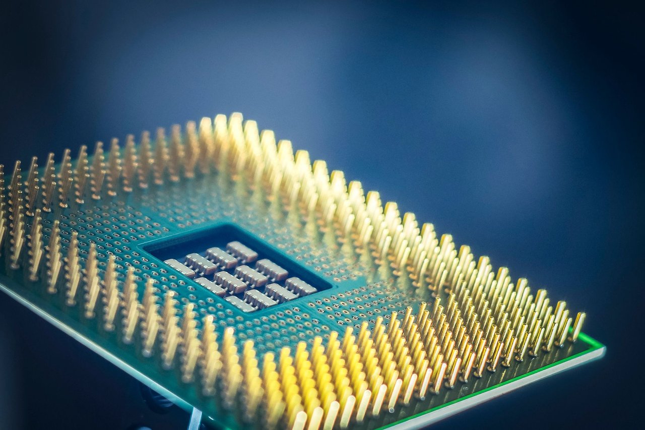 Close de um chip de processador com pinos dourados sobre fundo azul.
