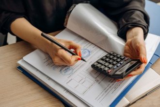 Contador usa uma calculadora e assina documentos financeiros sobre uma mesa de trabalho.
