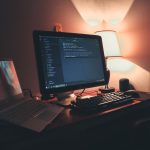 Espaço de trabalho com dois monitores exibindo códigos e ferramentas de programação, em um ambiente de escritório.
