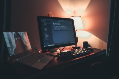 Espaço de trabalho com dois monitores exibindo códigos e ferramentas de programação, em um ambiente de escritório.