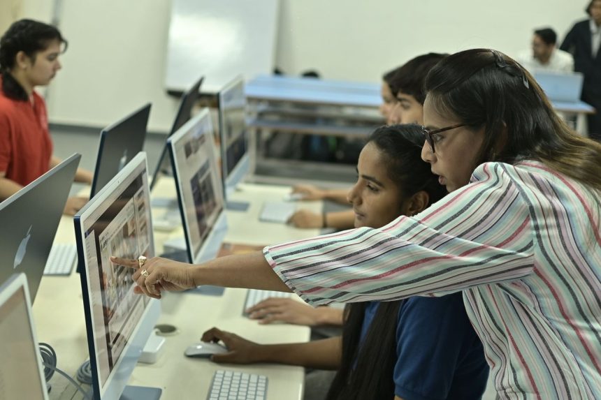 Professor e estudantes colaboram diante de computadores em um laboratório de informática.