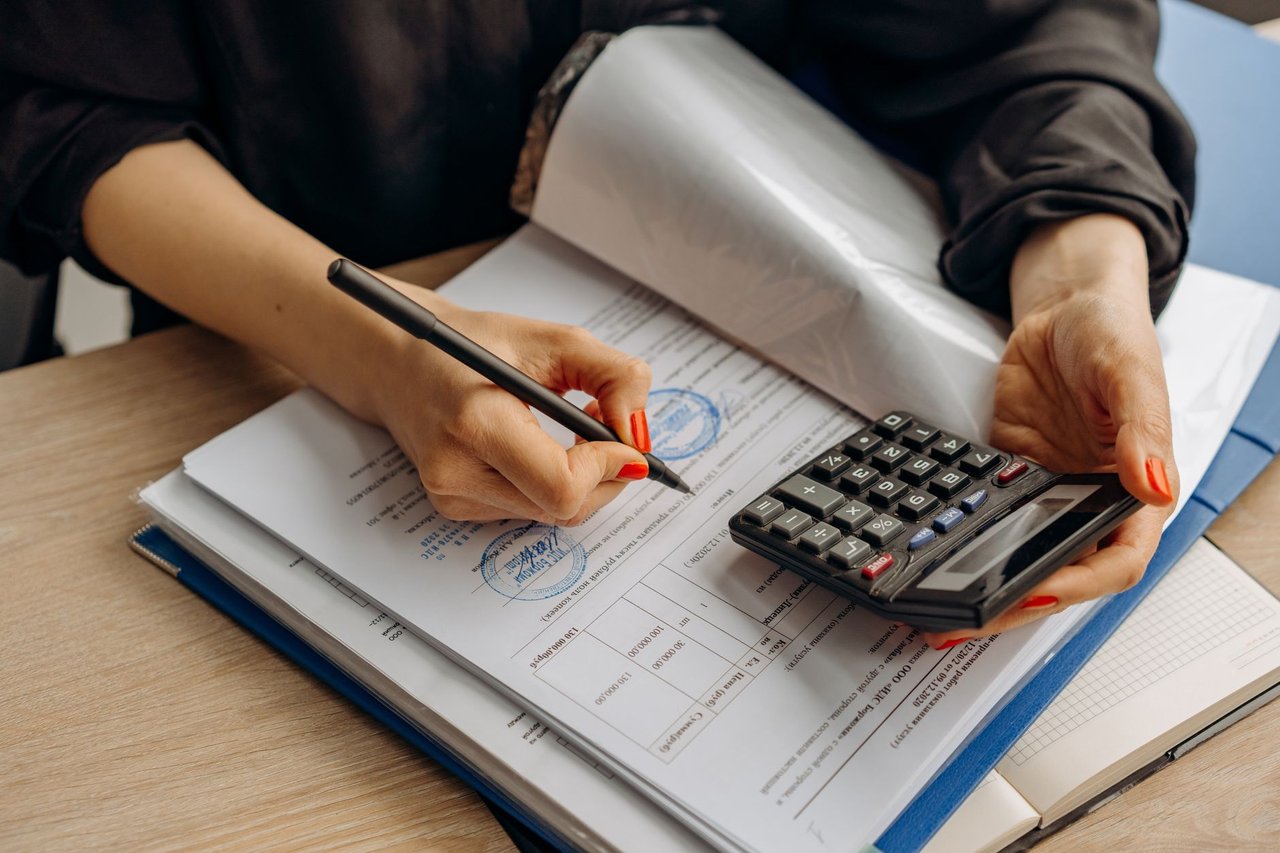 Contador usa uma calculadora e assina documentos financeiros sobre uma mesa de trabalho.